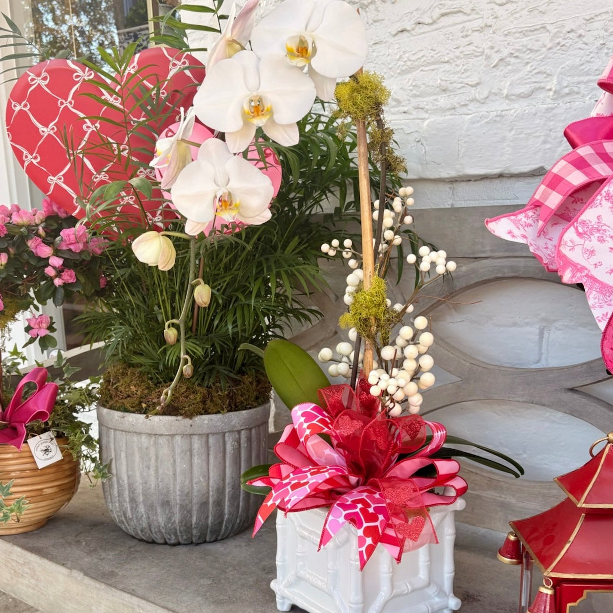 Decorative outdoor setting with potted plants, flowers, and a lantern on a stone surface.
