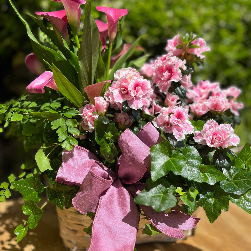 Arrangement of pink flowers with a pink bow on a wooden surface.