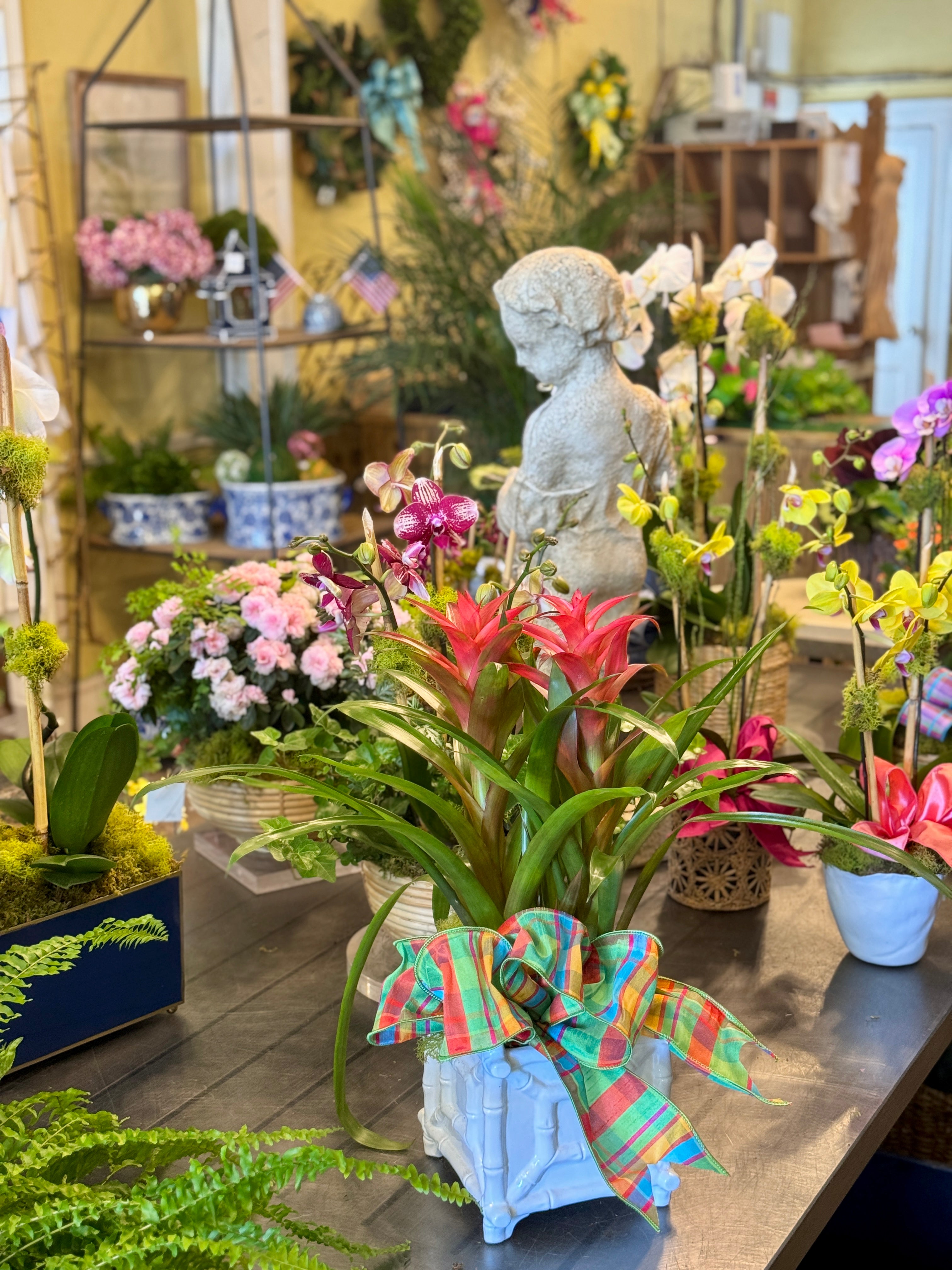 Floral arrangements with a colorful bow on a table in a garden center setting.
