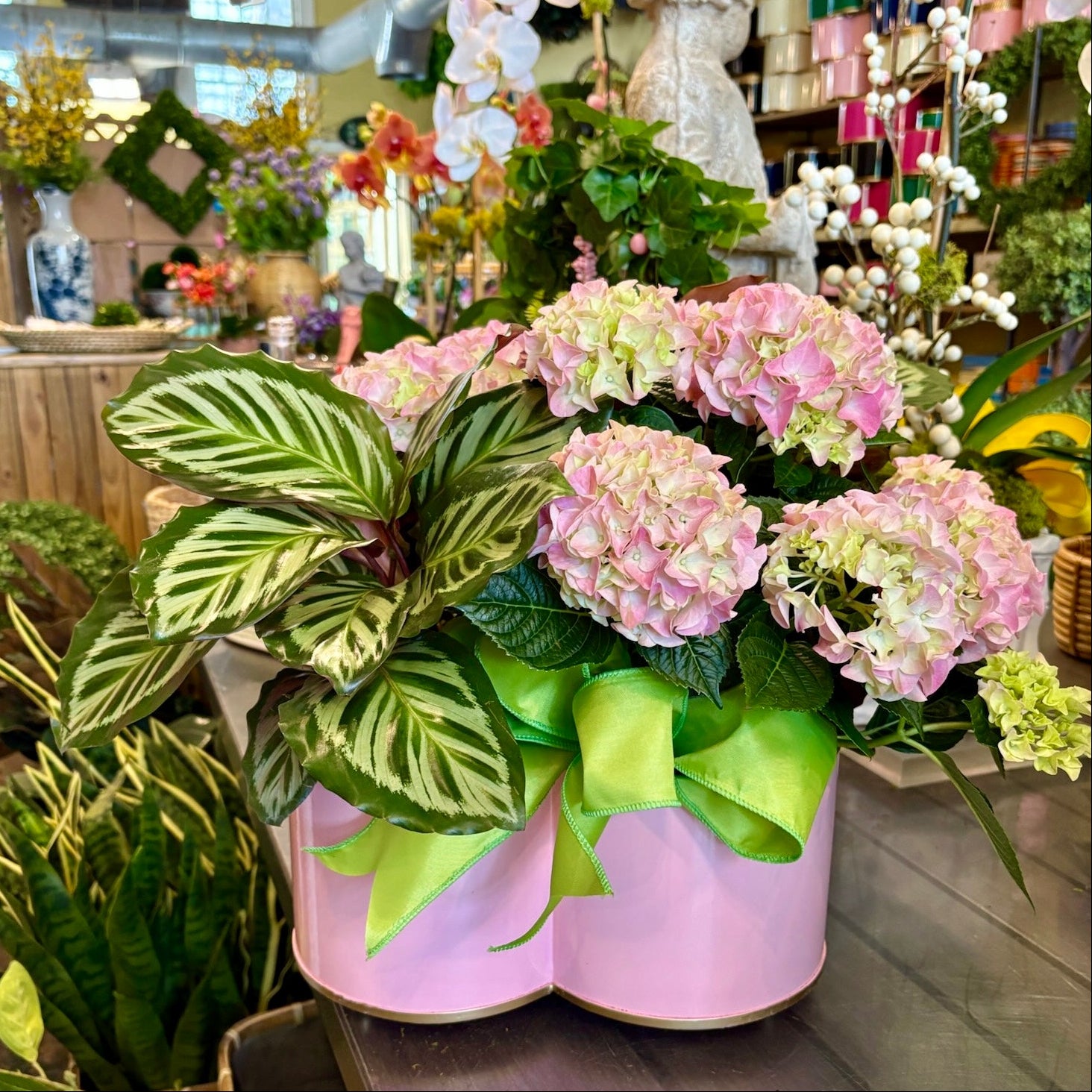 Decorative floral arrangement with pink flowers and green leaves in a store setting.