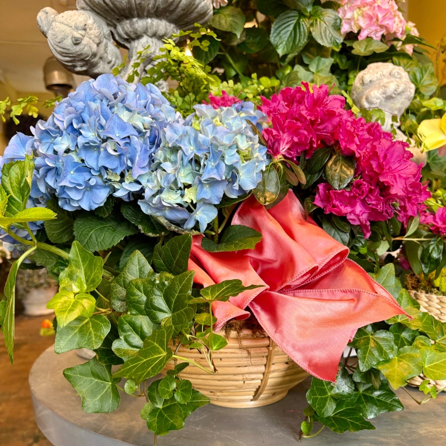 Arrangement of flowers with blue hydrangeas, pink azaleas, and green ivy on a store table.