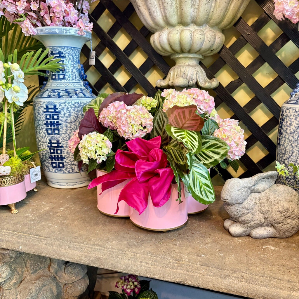 Decorative shelf with floral arrangements, vases, and a rabbit figurine against a lattice background.