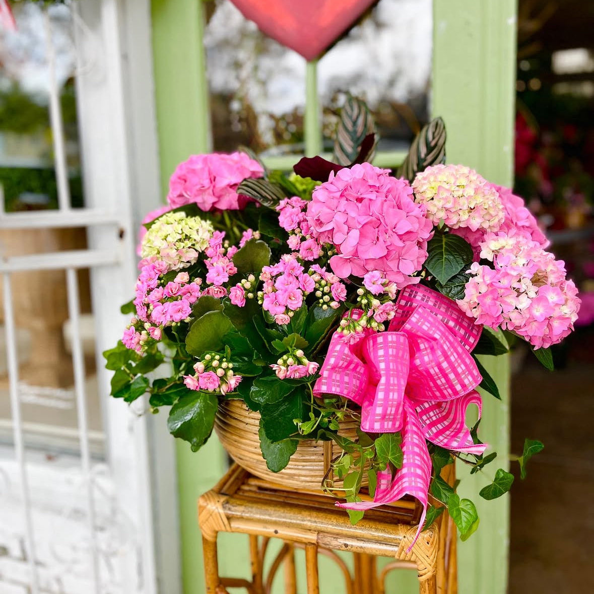 Arrangement of pink flowers with a decorative bow on a small table in front of a green door.