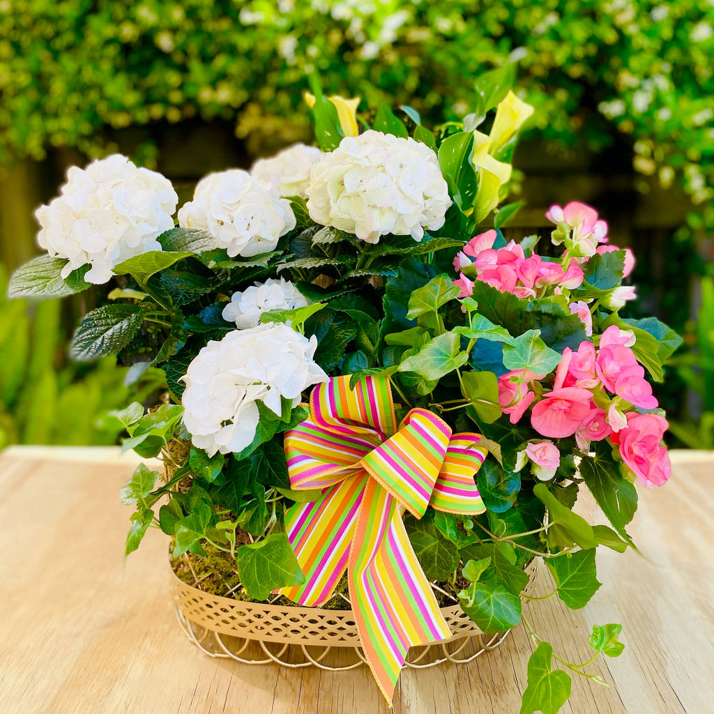 Floral arrangement with white and pink flowers and a colorful bow on a wooden surface.