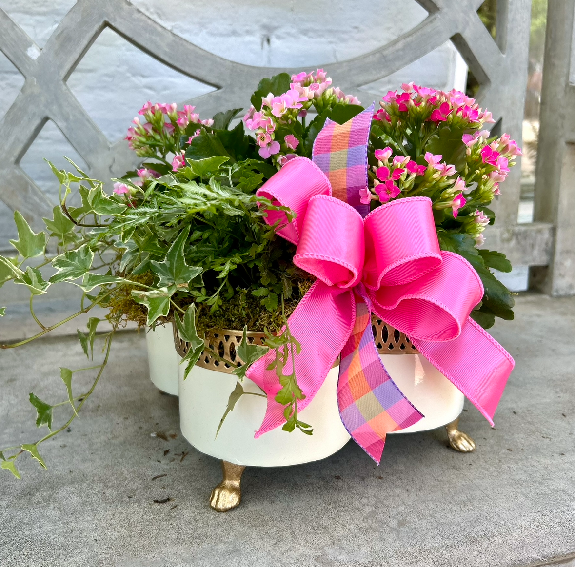 Floral arrangement in a decorative pot with a large pink bow on a concrete bench.