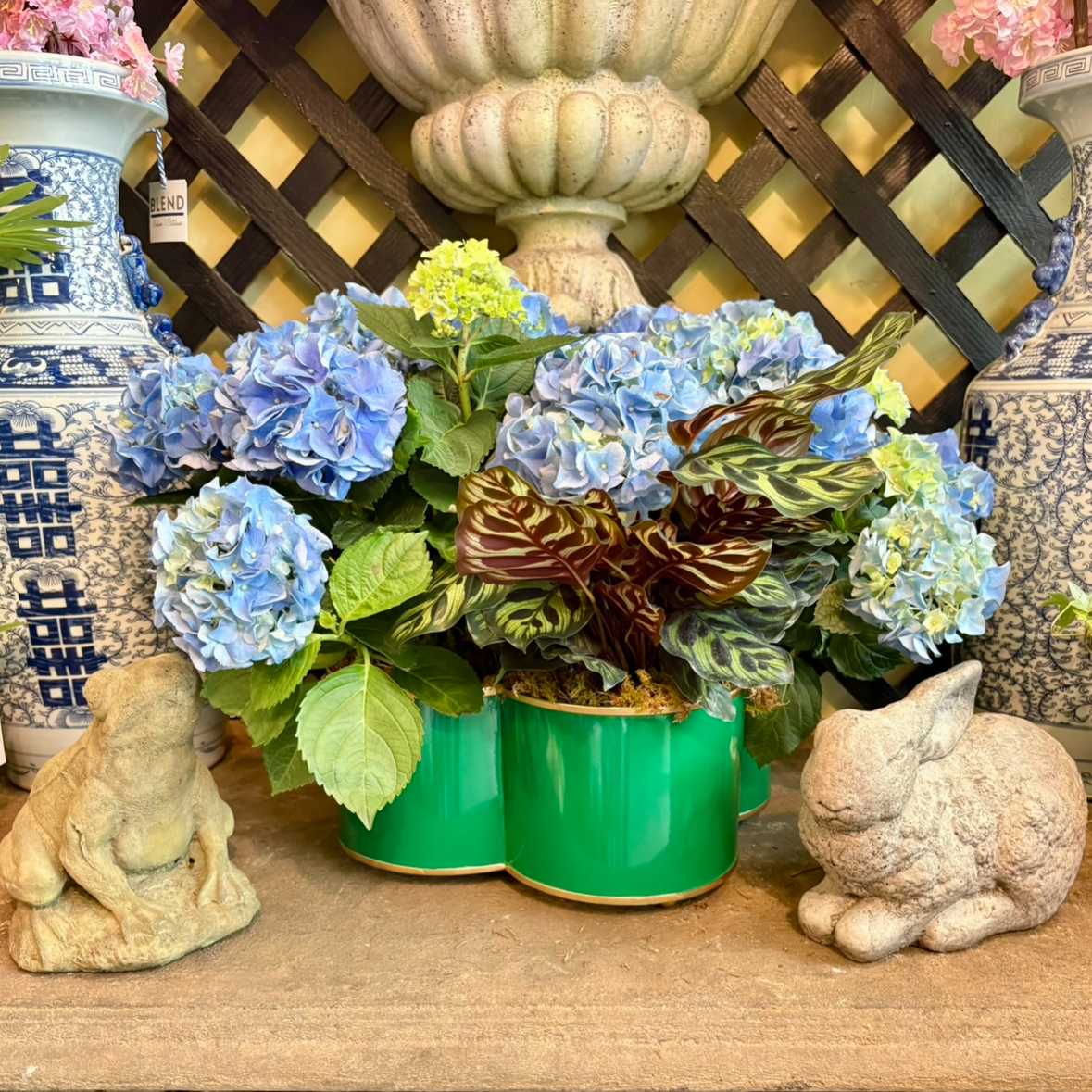 Decorative arrangement with flowers, a green planter, and decorative animals on a concrete surface.