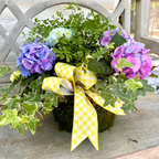 Floral arrangement with purple and blue flowers and a yellow bow on a concrete bench.